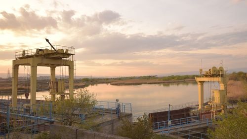 View of tower at riverbank against cloudy sky