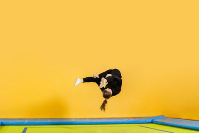 Side view of man jumping against yellow wall