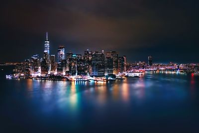 Illuminated buildings reflecting on river against sky at night