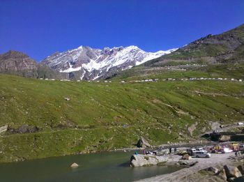 Cars parked by lake with rocky and snowcapped in background against clear sky