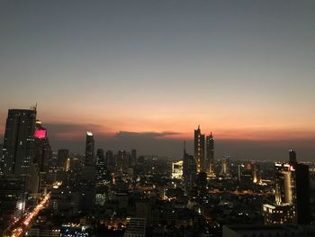 Illuminated buildings in city against sky during sunset