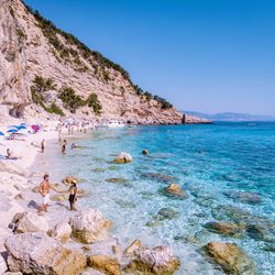 People on rocks at beach against clear blue sky