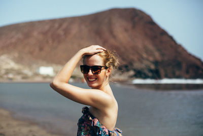 Portrait of smiling woman with hand in hair against mountains