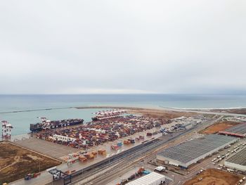 High angle view of cityscape by sea and commercial dock against sky