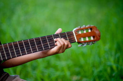 Cropped hand of person playing guitar over field