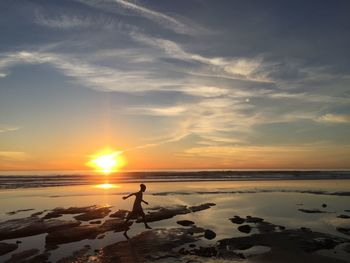 Silhouette girl running on beach against sky during sunset