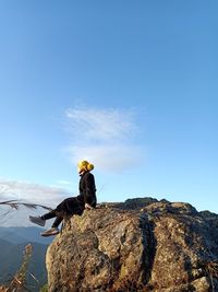 Man sitting on rock by mountain against sky