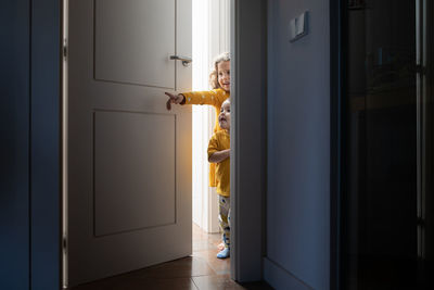 Charming brother and sister peeping out from door in modern apartment while having fun and looking away