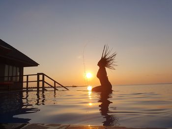 Silhouette woman tossing hair in sea against sky during sunset