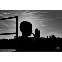 Silhouette boy photographing against sky during sunset