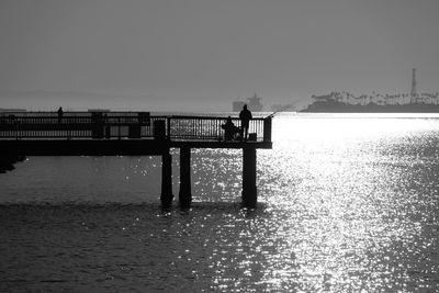 Silhouette man on pier over sea against clear sky