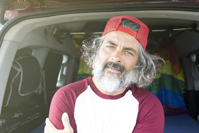 Handsome man in cap sitting in car trunk looking at camera. warm travel concept image