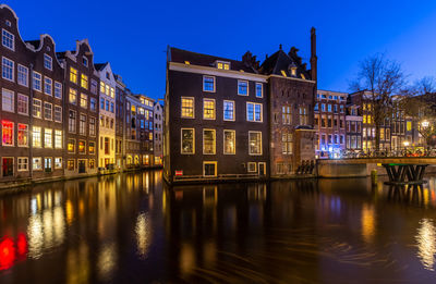 Illuminated buildings by river against sky at night