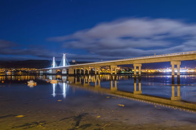 Illuminated bridge over river against sky at night