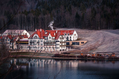 Houses by river and buildings against trees