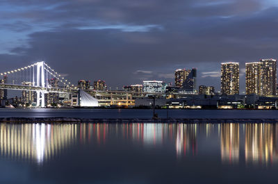 Illuminated city by river against sky