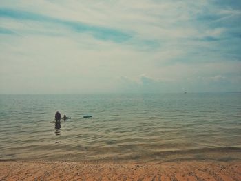 Man standing in sea against cloudy sky