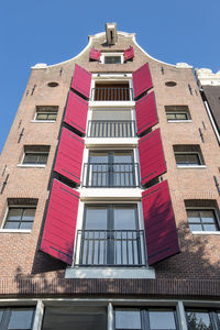 Low angle view of red shutters on a canal house in amsterdam against blue sky