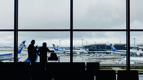 Rear view of people standing at airport against sky