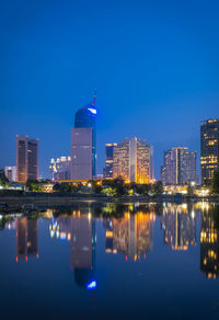 Reflection of illuminated buildings in lake against blue sky at night