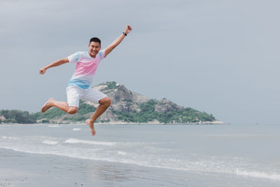 Full length of man jumping at beach against sky