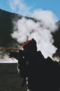 Side view of photographer against smoke on sunny day