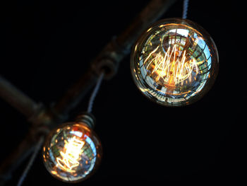 Low angle view of illuminated light bulb hanging against black background