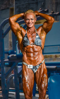 Portrait of smiling female body builder standing against equipment