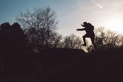 Silhouette man jumping on bare tree against sky