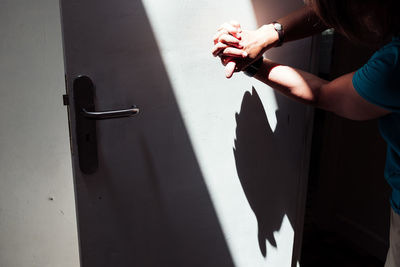 Cropped hands of woman making chicken shadow puppet over white door