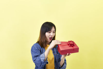 Young woman holding box against yellow background