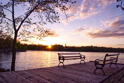 Bench by lake against sky during sunset