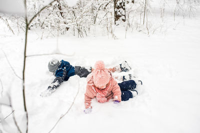 High angle view of kids lying on snow covered land during winter