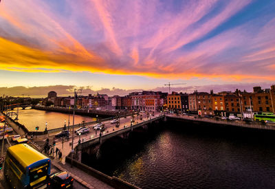 Bridge over river amidst buildings against sky during sunset