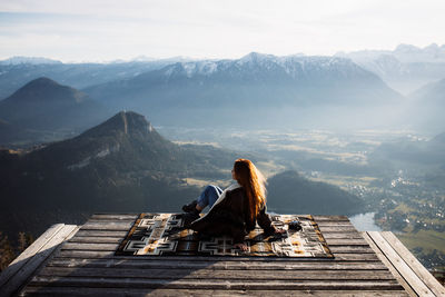 Rear view of people sitting on mountain against sky