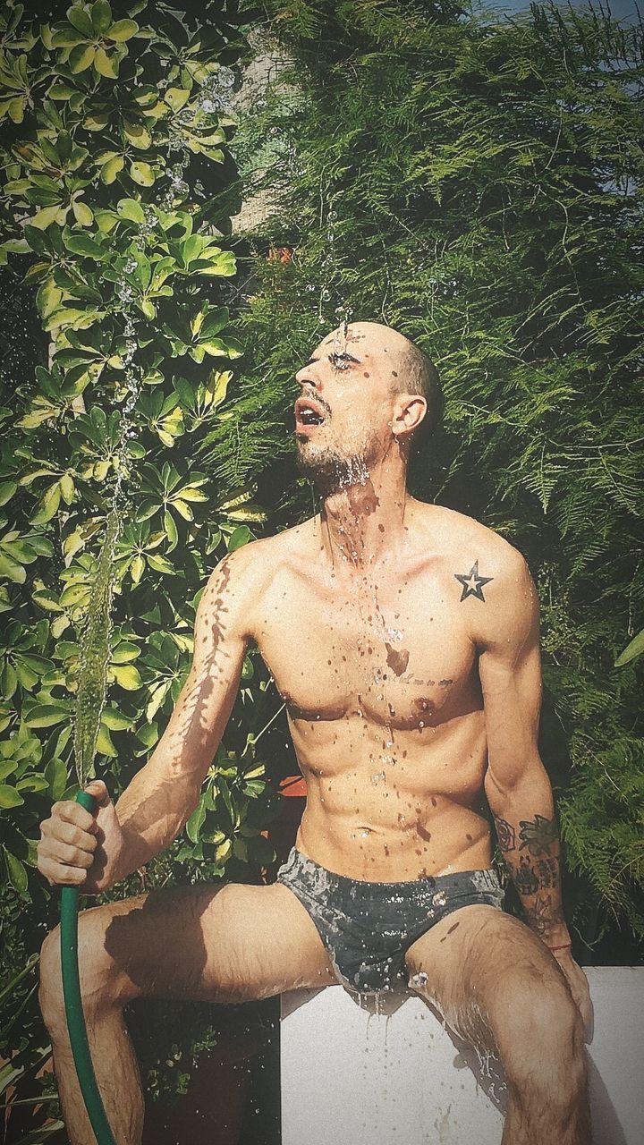 shirtless, one person, young men, front view, real people, young adult, lifestyles, plant, leisure activity, three quarter length, nature, men, day, tree, tattoo, outdoors, front or back yard, standing, shorts