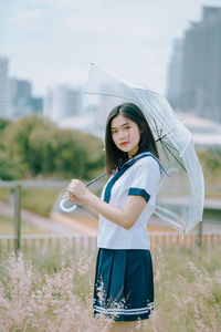 Portrait of young woman with umbrella standing amidst plants on field