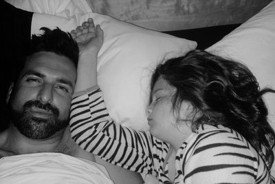 High angle portrait of father lying by sleeping daughter on bed at home