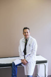 Portrait of smiling doctor sitting on bed against wall