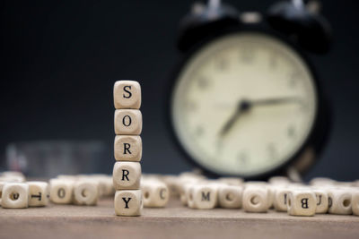 Close-up of sorry text made with toy blocks against alarm clock on wooden table