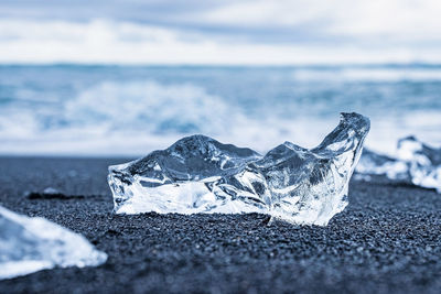 Close-up of shiny ice chunk on black sand shore of diamond beach