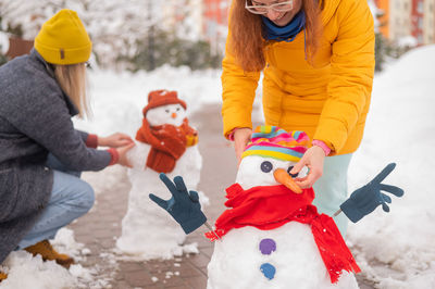 Two faceless caucasian women are making a snowman. girlfriends have fun in winter
