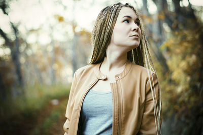 Thoughtful young woman with dreadlocks looking away at public park