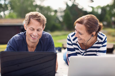 Smiling mature couple using laptops while lying on pier