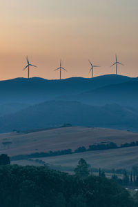 Wind turbines on land against sky during sunset