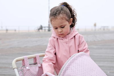 Young girl playing with her toy stroller on the boardwalk