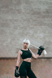 Portrait of woman with boxing gloves standing against wall