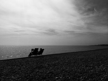 Silhouette people sitting chair at beach against sky