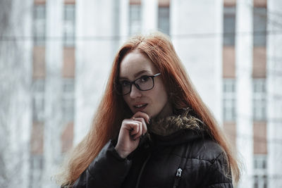 Portrait of thoughtful young woman standing against building in city