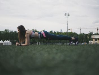 Side view of woman lying on grass against sky